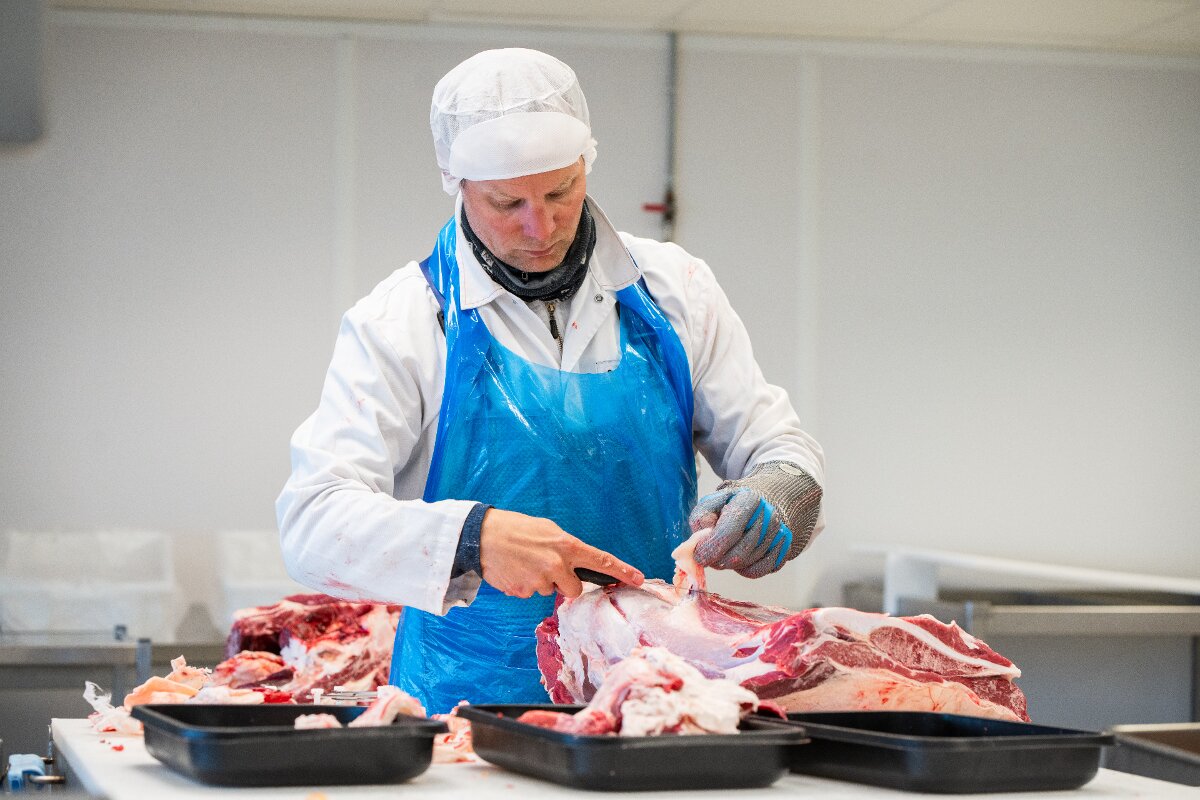 En kjøttskjærer i beskyttelsesklær skjærer i et kjøttstykke.